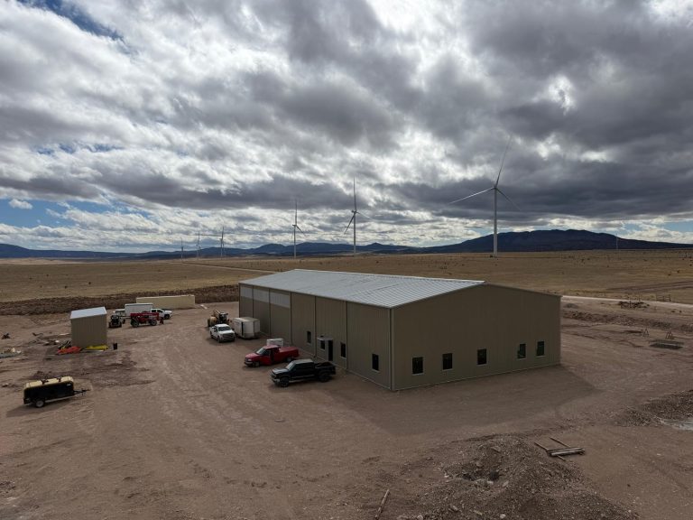Tan steel shop and office building with wind turbines in the distance