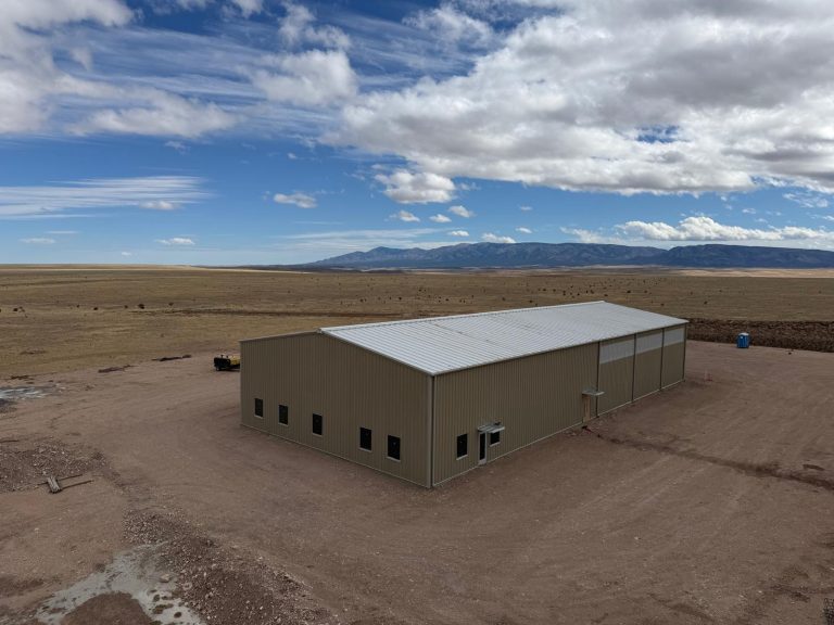 Tan steel building with a row of windows on open prairie, with mountains in the distance