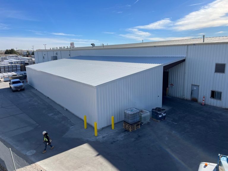 White steel building addition beside a large industrial plant