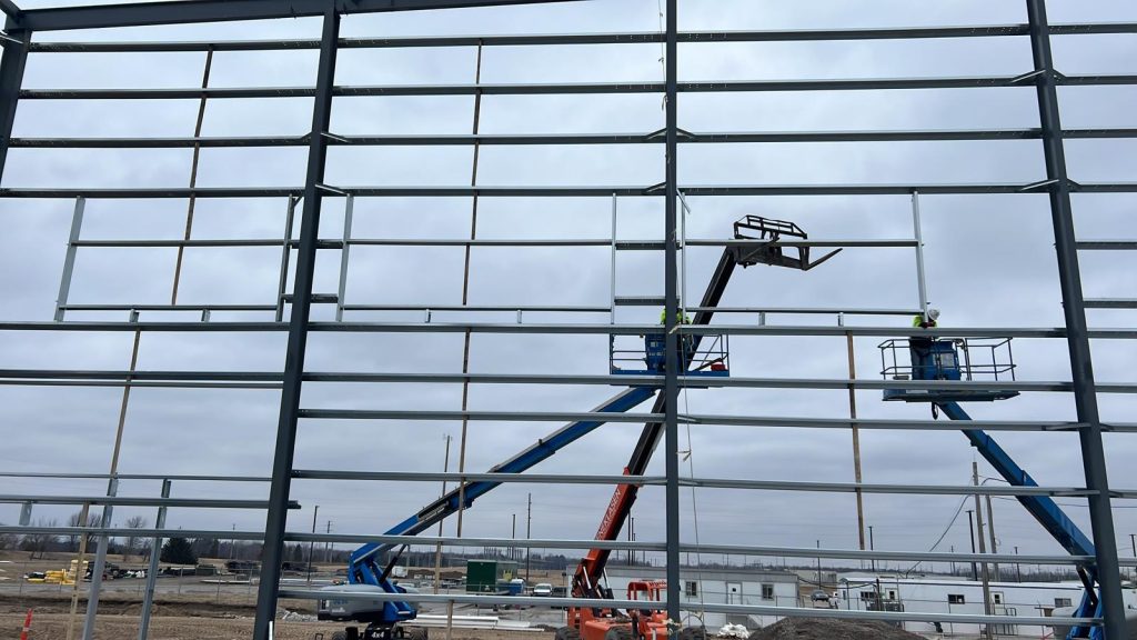 Two boom lifts with crews installing girts on a tall steel wall