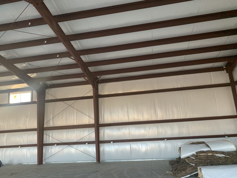 Inside a steel building: red-oxide frames and purlins over white roof insulation