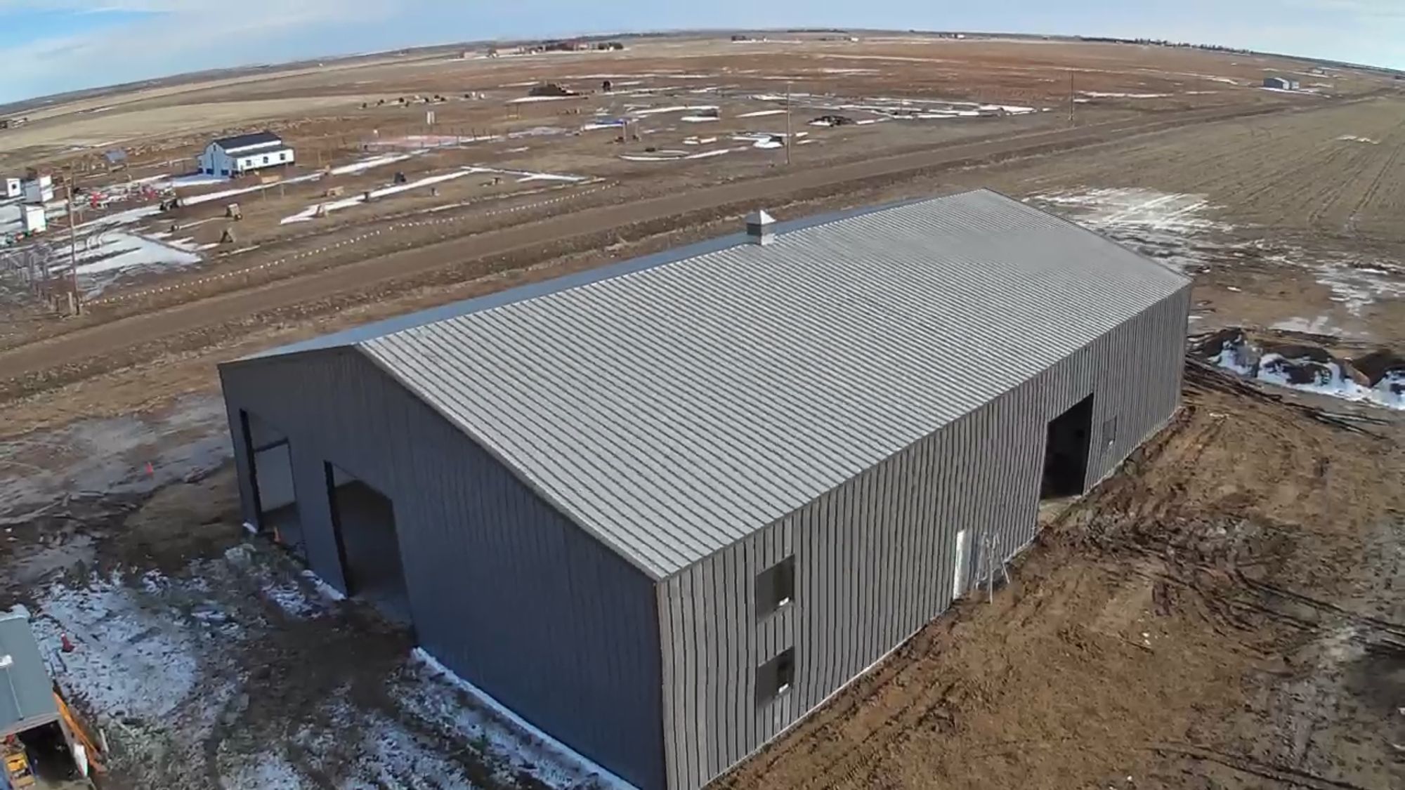 Aerial view of a large gray steel shop with open door and window openings on flat farmland near Byers, Colorado