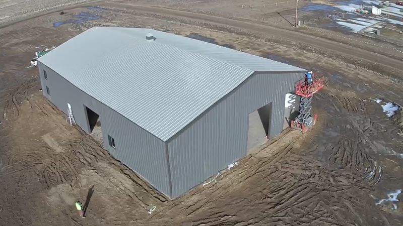 Aerial view of a gray steel shop with a walk door, windows and a large door opening, on a graded lot near Byers, Colorado
