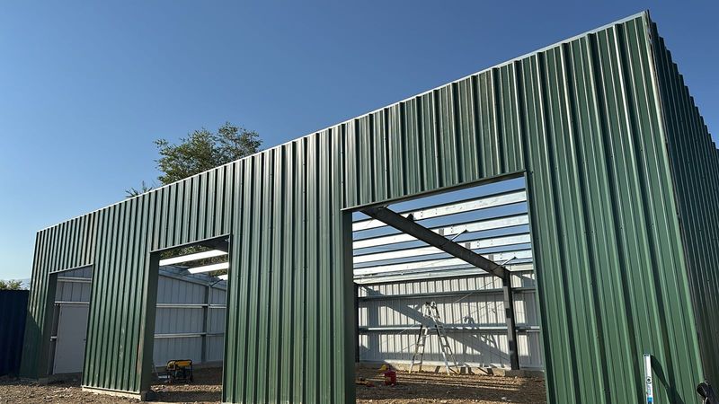 Green steel equipment shed with its wall panels on and open bays showing the steel framing inside, near Longmont, Colorado