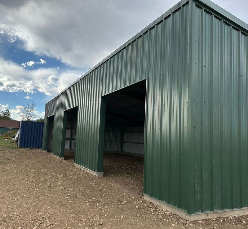 Green steel equipment shed with three open bays seen from the side, with mountains behind, near Longmont, Colorado