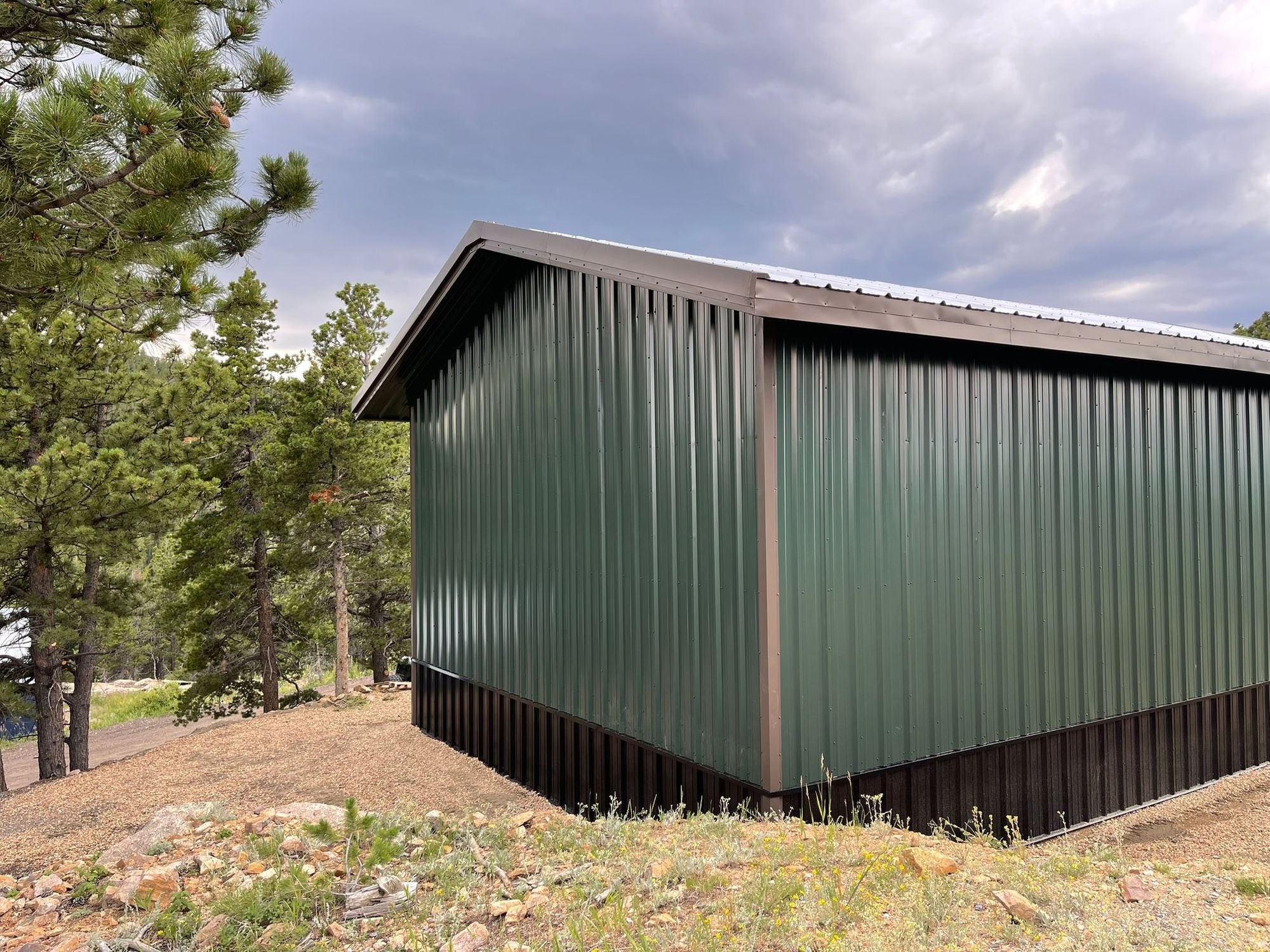 Green steel shop with brown trim and a dark wainscot among pines near Golden, Colorado