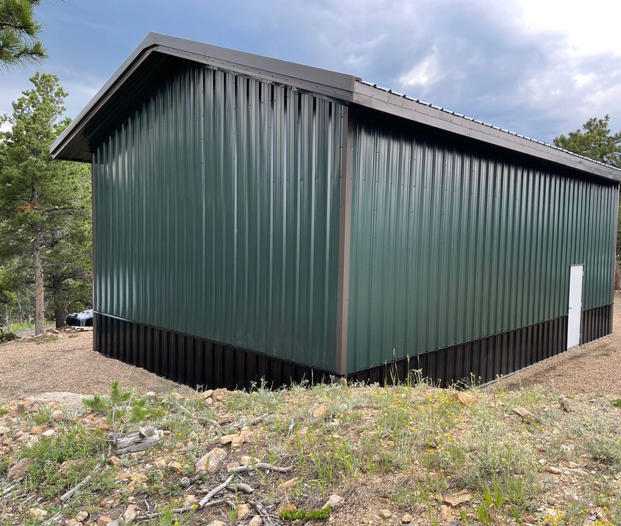 Green steel shop with brown trim, a dark brown wainscot and a white walk door among pines near Golden, Colorado