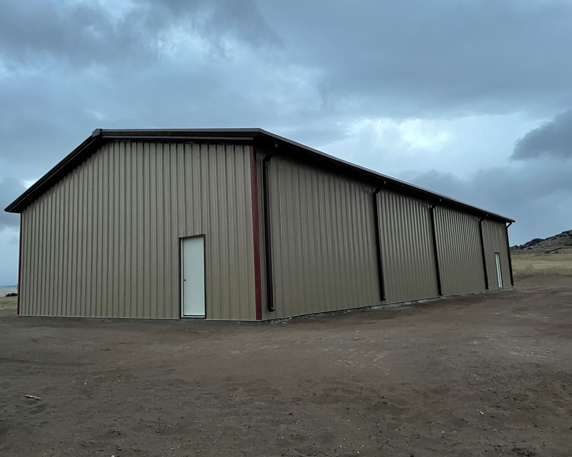 Long tan steel shop with brown trim, gutters and downspouts near Westcliffe, Colorado