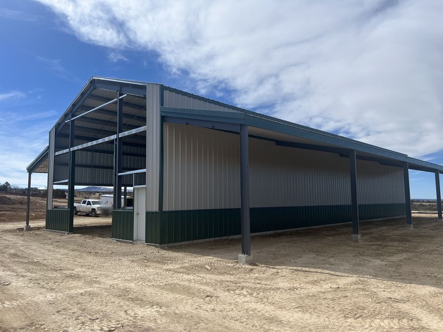 Long open-sided steel lean-to with dark columns along a cream barn wall with a green wainscot, near Hotchkiss, Colorado