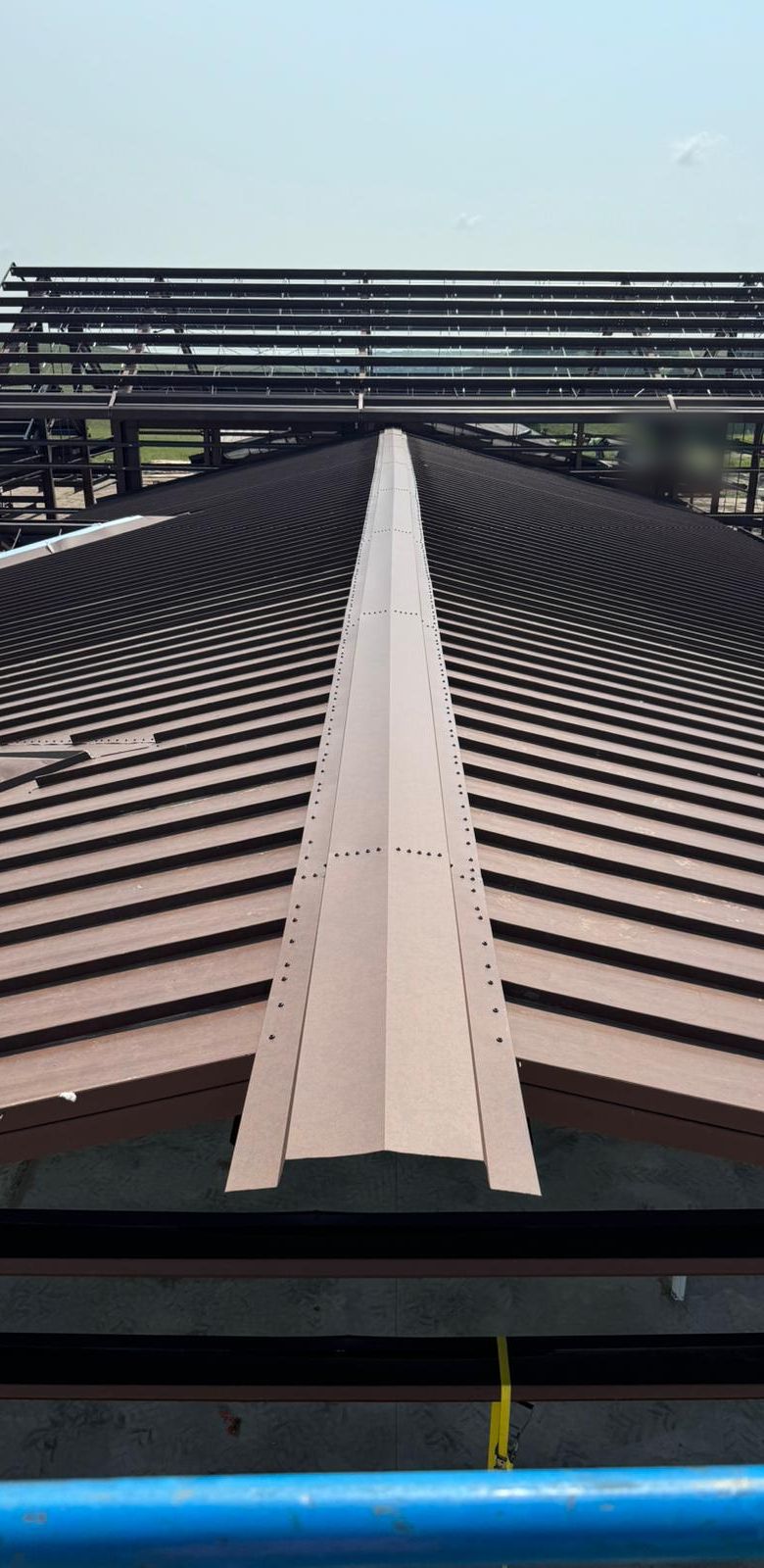 Ridge cap along a brown standing-seam roof, with bare steel frames beyond, near Mullen, Nebraska