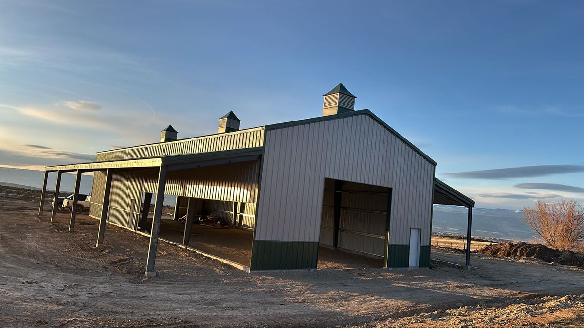 Steel barn at dusk with a tall end-wall door opening, cupolas on the ridge and a long lean-to, near Hotchkiss, Colorado