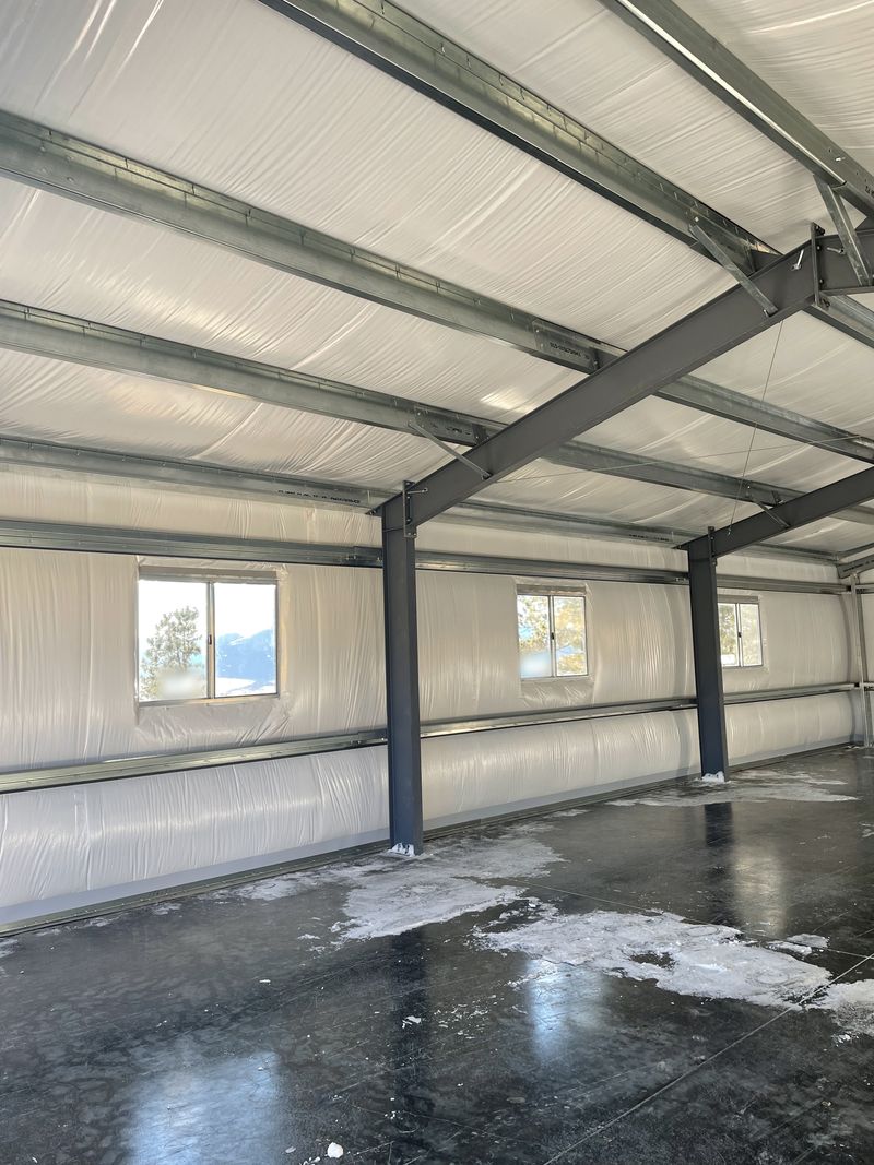 Inside a steel shop: white-faced insulation on the walls and roof, galvanized purlins and girts, dark steel frames and sliding windows, near Westcliffe, Colorado