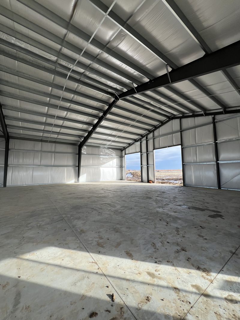 Inside a steel shop looking up at dark frames, galvanized purlins, diagonal strap bracing and white-faced insulation, near Byers, Colorado
