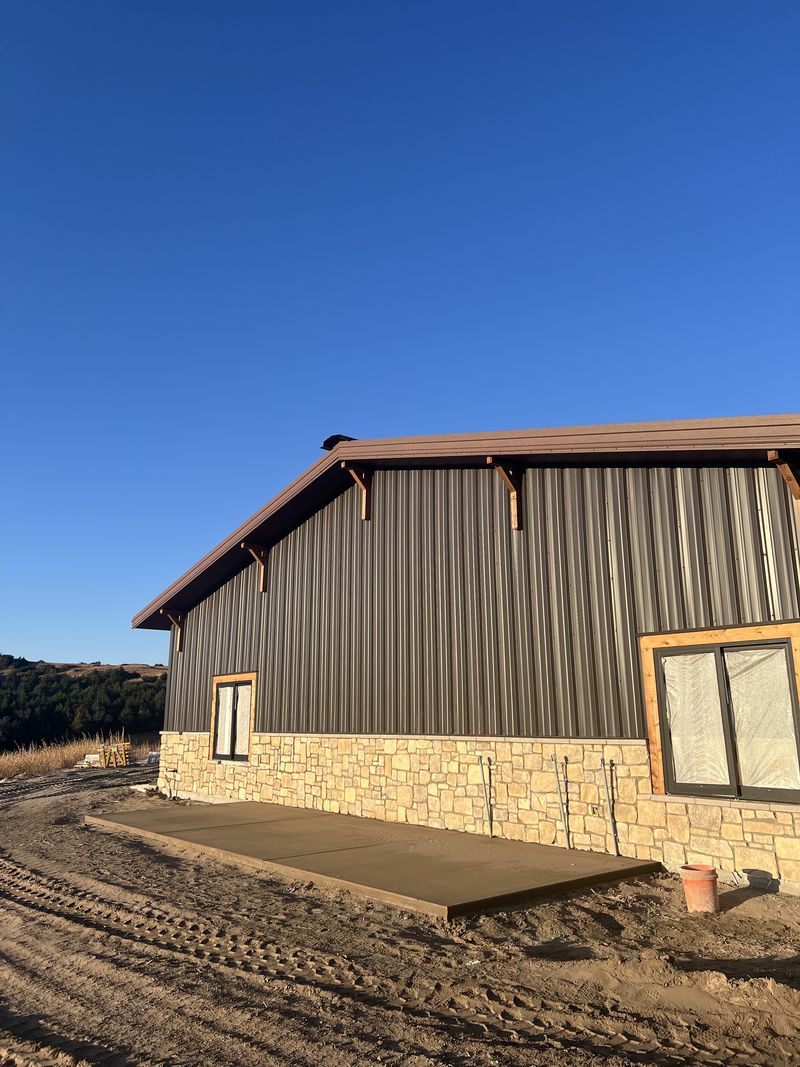 Dark steel wall over stone wainscot with timber-style brackets under the roof edge near Mullen, Nebraska