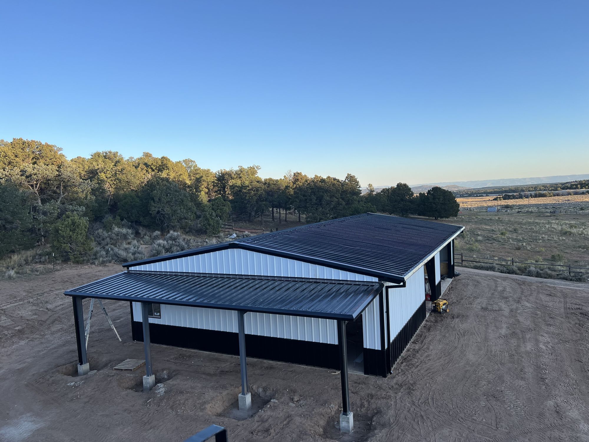 White steel building with black wainscot, a black roof and a covered porch in Glade Park, Colorado