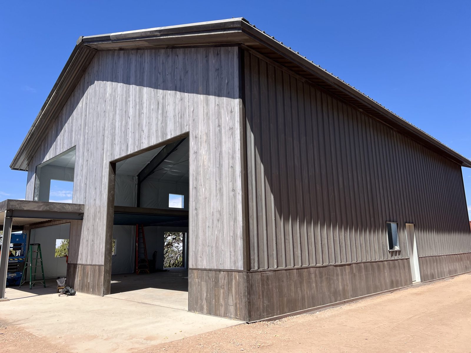 Steel barndominium with wood-look siding, a darker wainscot and a tall door opening