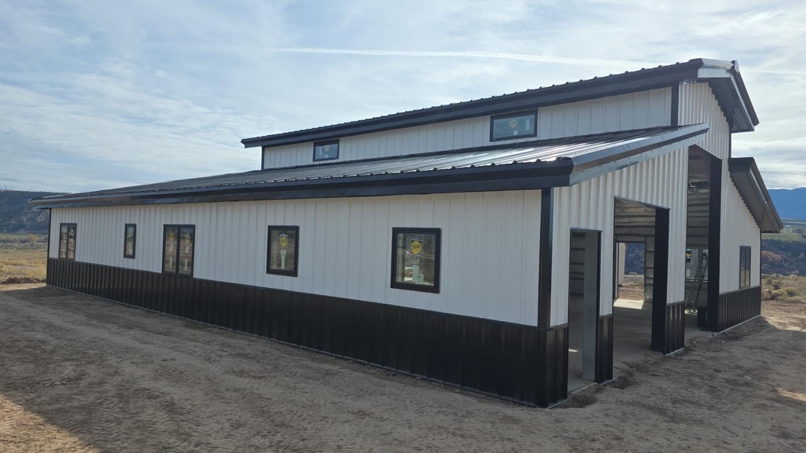 White monitor-style steel barn with a raised center roof, windows along the upper and lower walls and a black wainscot